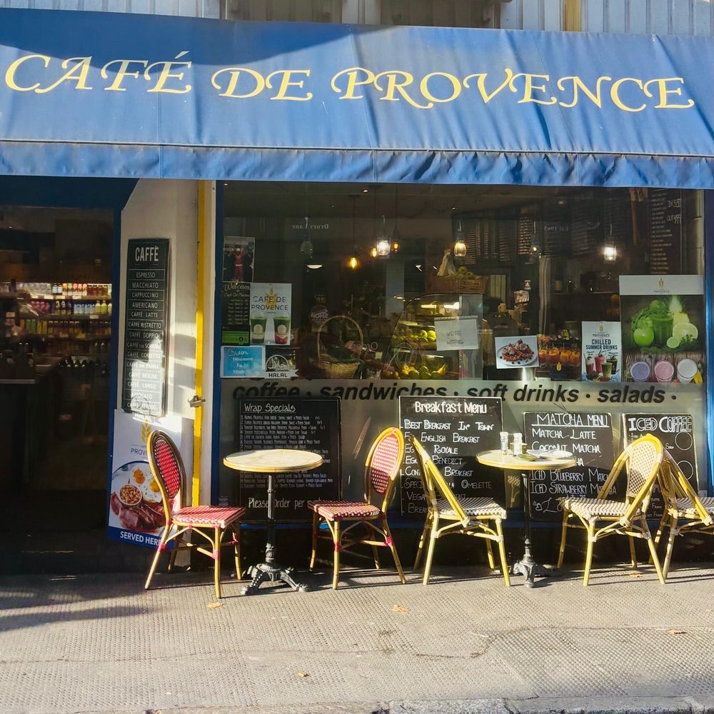 The shopfront of Cafe de Provence on Drury Lane, with its blue awning, window display and pavement tables with rattan chairs