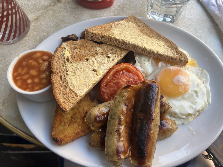 A full English breakfast plate with sausages, fried egg, beans, tomato and toast
