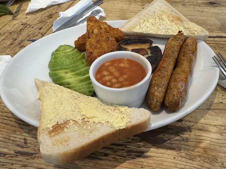 A vegetarian breakfast plate with hash browns, avocado, veggie sausages, beans and toast